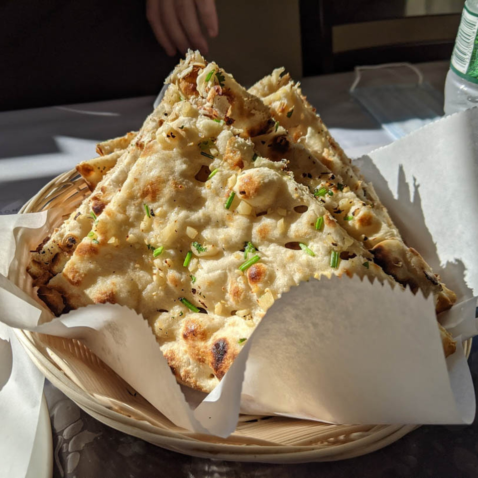 Basket of freshly baked garlic naan bread, garnished with green herbs, from Good Luck Restaurant.