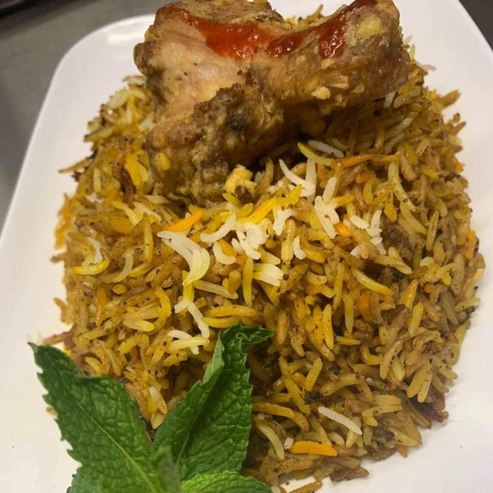 Nepalese chicken biryani with a drumstick topped with red sauce and a mint garnish.